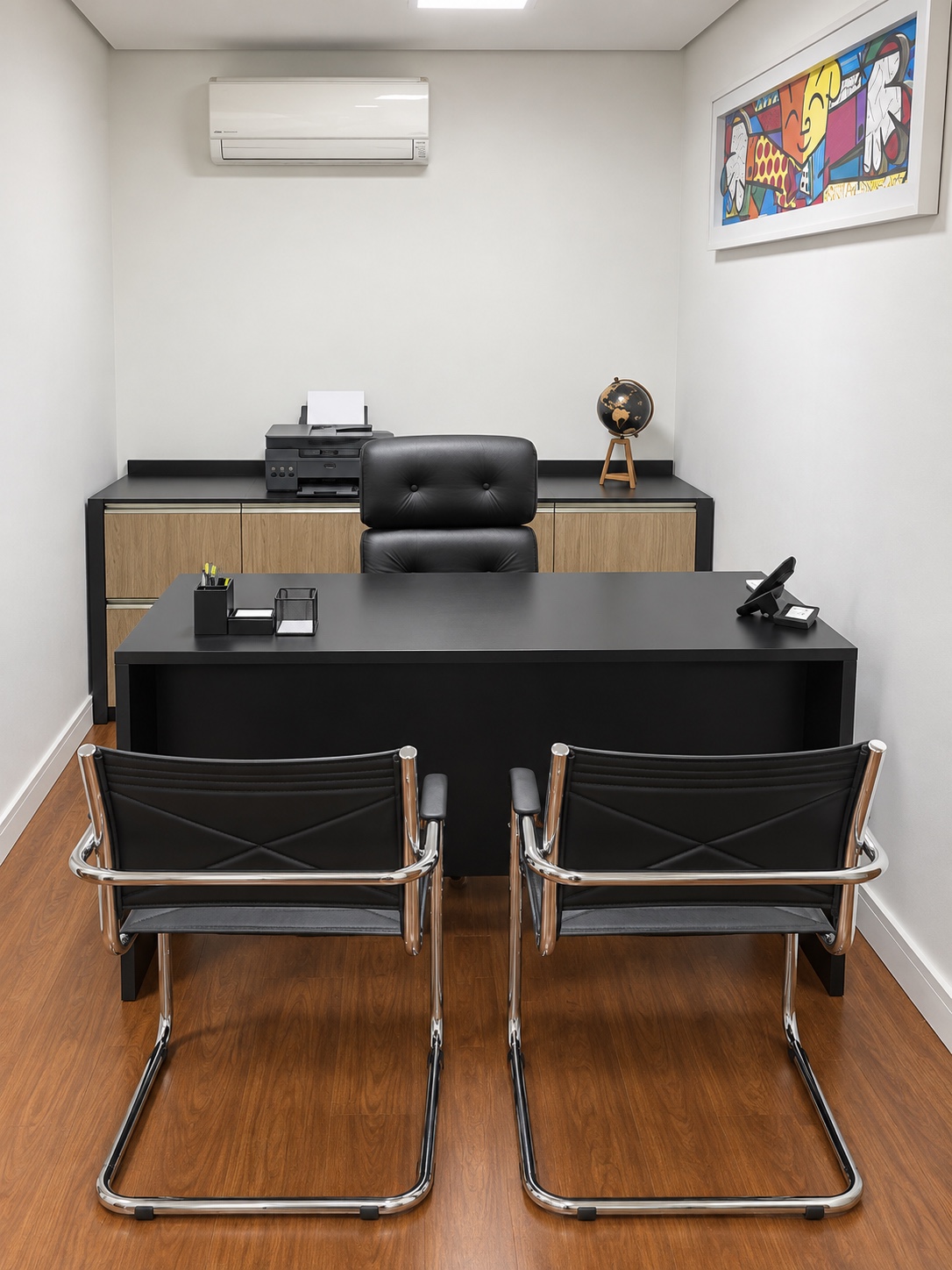 Sala de atendimento com mesa preta, duas cadeiras para visitantes e impressora ao fundo